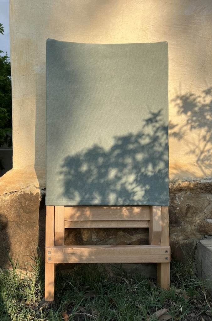 Beech wood folding chair with olive canvas against a sunlit wall